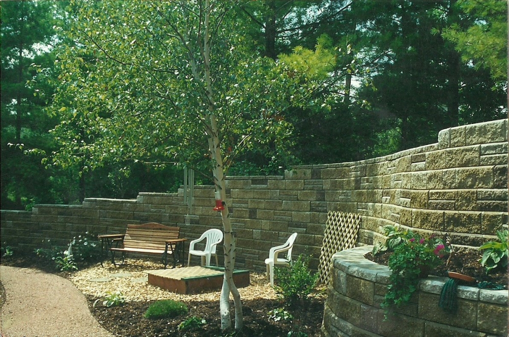 A high retaining wall surrounds a patio and fire pit